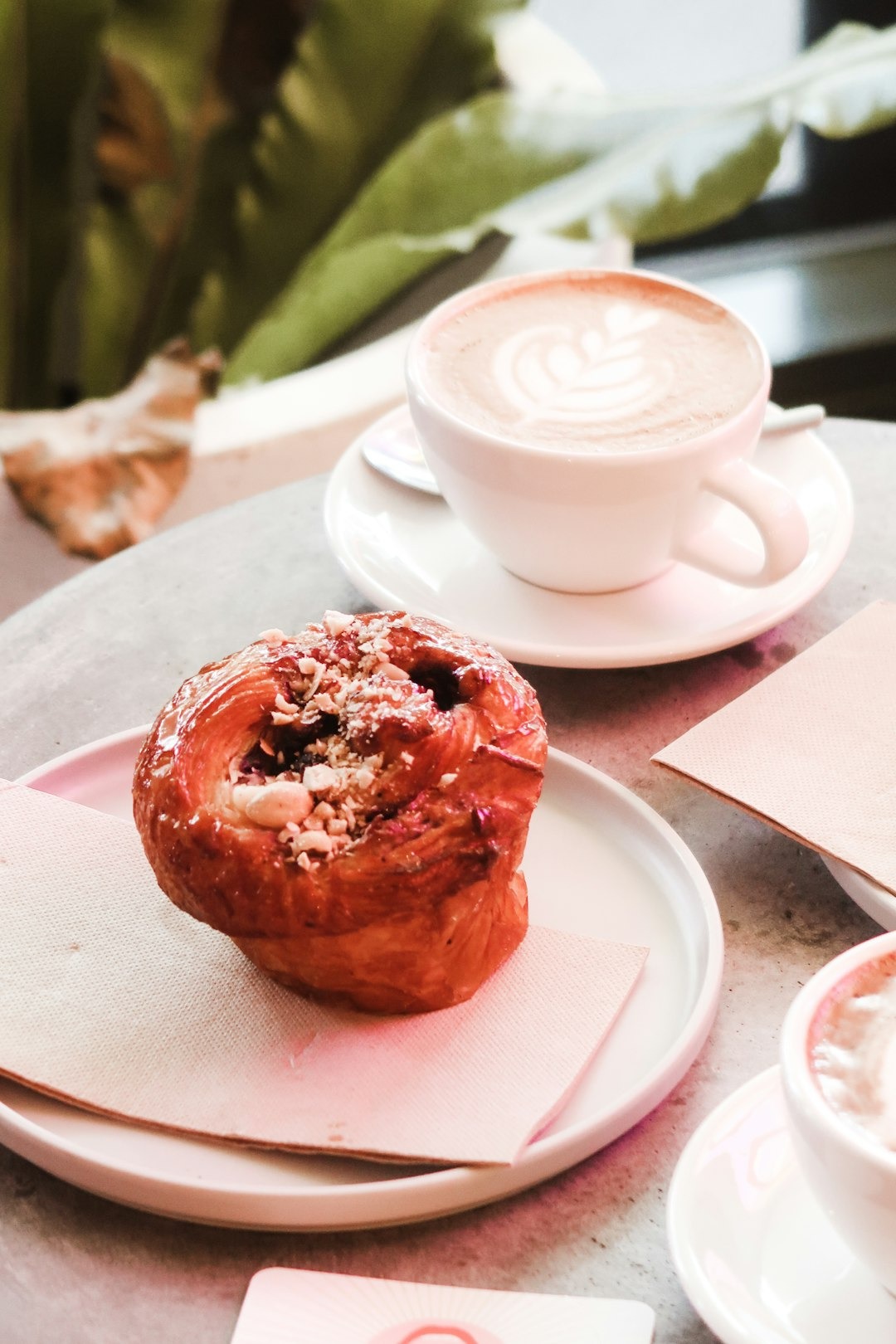 Cappuccino with latte art and a nut-topped pastry on cafe tables.